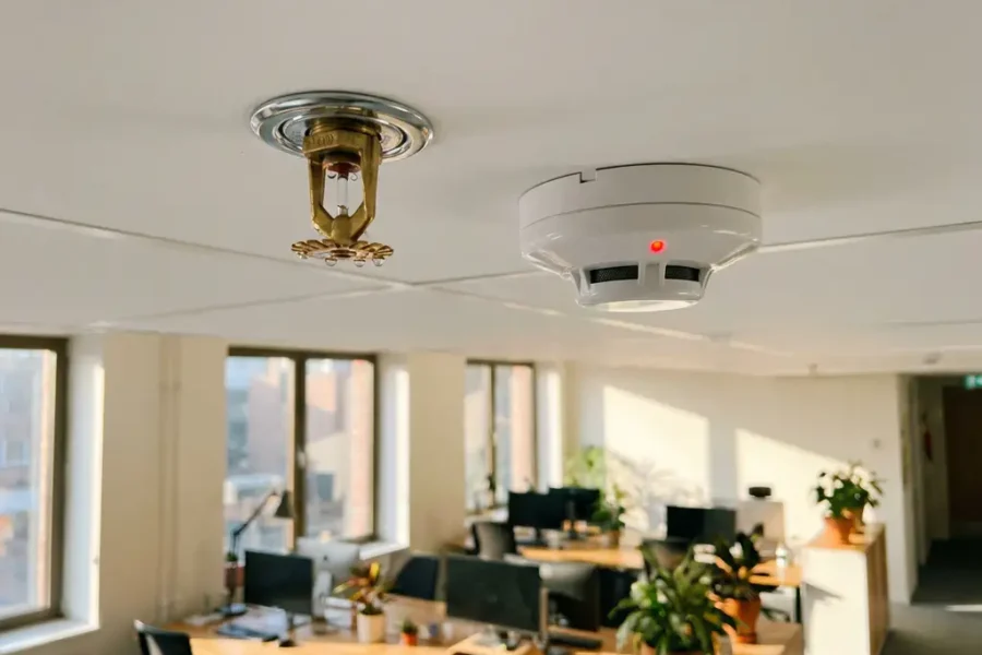 Moderne plafond-geïnstalleerde brandsprinkler en rookmelder op wit commercieel plafond in professionele kantooromgeving
