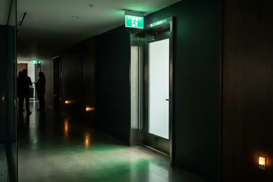 Groene nooduitgang verlichting schijnt boven moderne kantoor deuropening tijdens stroomuitval op gepolijste betonvloer