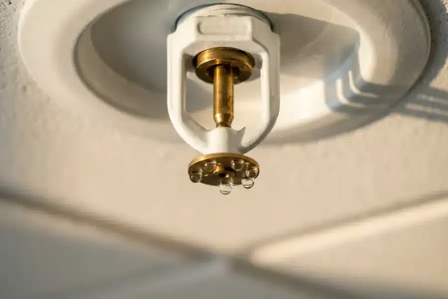 Wit plafond sprinklerkop met waterdruppels aan messing mondstuk in kantooromgeving met natuurlijk daglicht