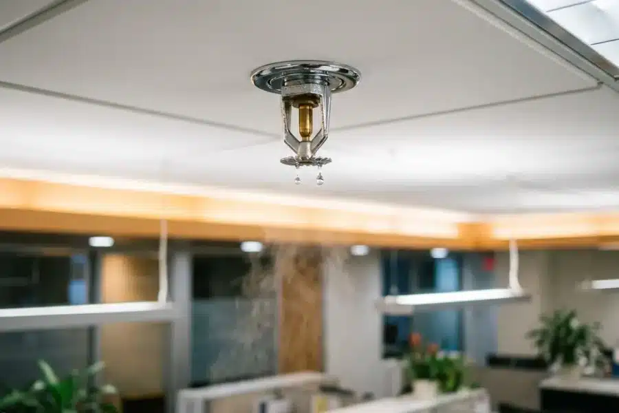 Moderne brandsprinkler aan wit kantoorplafond met waterdruppels die zich vormen aan de sproeikop